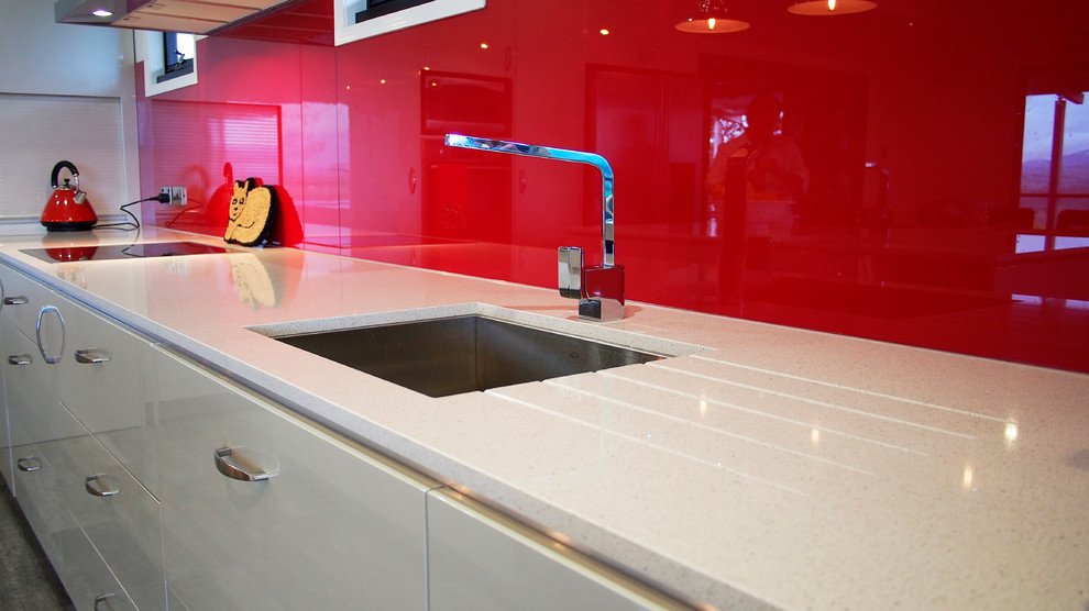 Mid-sized contemporary l-shaped eat-in kitchen in Brisbane with an undermount sink, flat-panel cabinets, beige cabinets, quartz benchtops, red splashback, glass sheet splashback, stainless steel appliances and with island.
