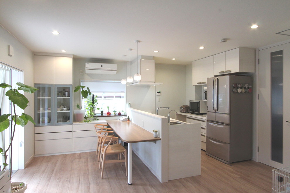 Photo of a galley open plan kitchen in Other with an undermount sink, light wood cabinets, solid surface benchtops, white splashback, stainless steel appliances, plywood floors and a peninsula.