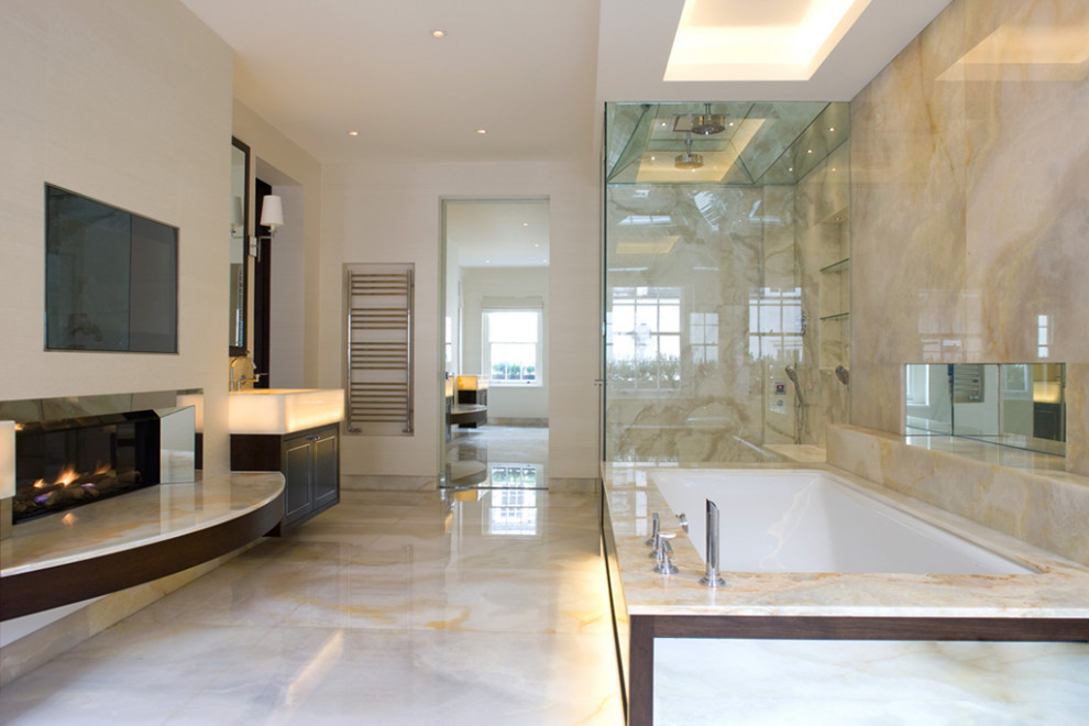 This is an example of a large contemporary master bathroom in London with beaded inset cabinets, brown cabinets, an undermount tub, an open shower, beige tile, marble, beige walls, marble floors, a wall-mount sink, onyx benchtops, beige floor, a hinged shower door, beige benchtops, an enclosed toilet, a double vanity and a floating vanity.