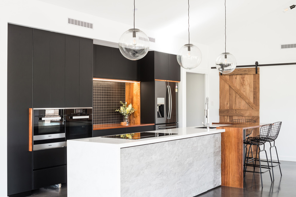Inspiration for a mid-sized contemporary galley open plan kitchen in Hobart with an undermount sink, black cabinets, solid surface benchtops, black splashback, ceramic splashback, stainless steel appliances, concrete floors, with island, grey floor, white benchtop and flat-panel cabinets.