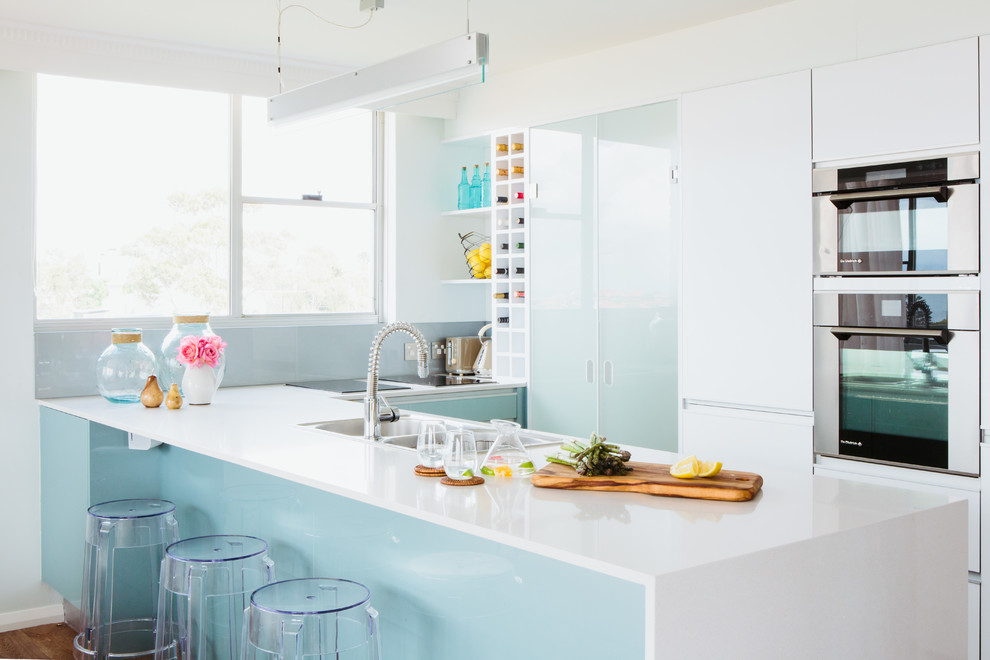 This is an example of a small beach style kitchen in Sydney with a double-bowl sink, granite benchtops, stainless steel appliances, light hardwood floors, flat-panel cabinets and a peninsula.