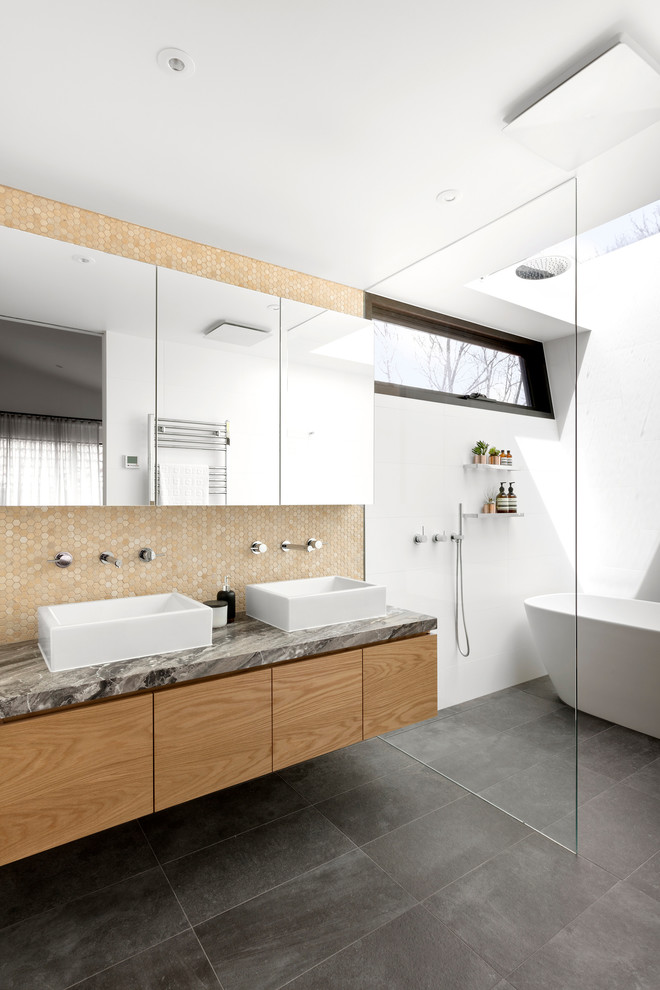Photo of a mid-sized contemporary master bathroom in Melbourne with flat-panel cabinets, medium wood cabinets, a freestanding tub, an open shower, a wall-mount toilet, white tile, ceramic tile, white walls, porcelain floors, a vessel sink, marble benchtops, grey floor and an open shower.