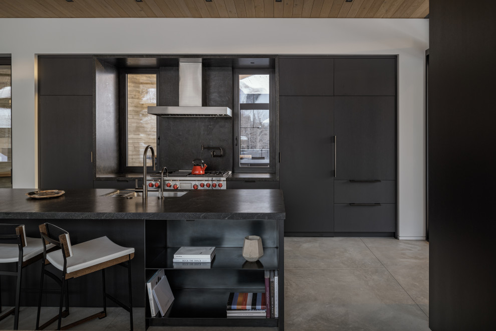 Country galley open plan kitchen in Other with an undermount sink, flat-panel cabinets, black cabinets, black splashback, stainless steel appliances, concrete floors, with island, grey floor, black benchtop and wood.