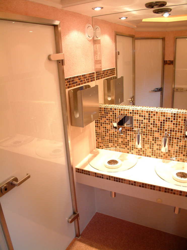 Klassisk inredning av ett stort beige beige toalett, med en vägghängd toalettstol, brun kakel, glaskakel, beige väggar, linoleumgolv, ett fristående handfat, bänkskiva i glas och orange golv