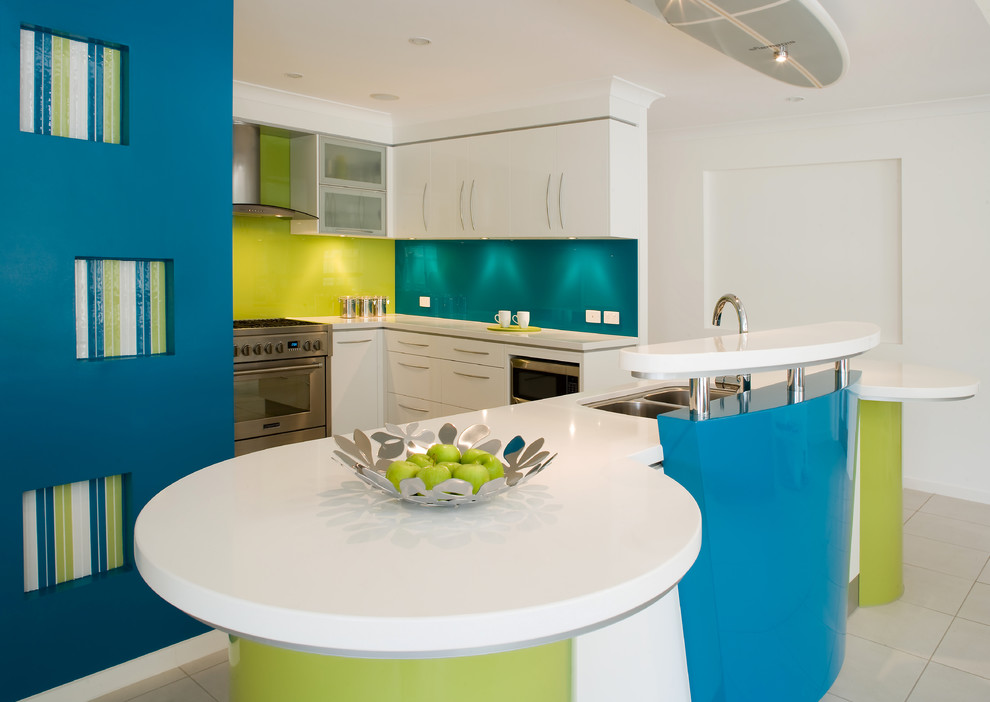 This is an example of a contemporary kitchen in Brisbane with a double-bowl sink, flat-panel cabinets, white cabinets, green splashback, glass sheet splashback and stainless steel appliances.