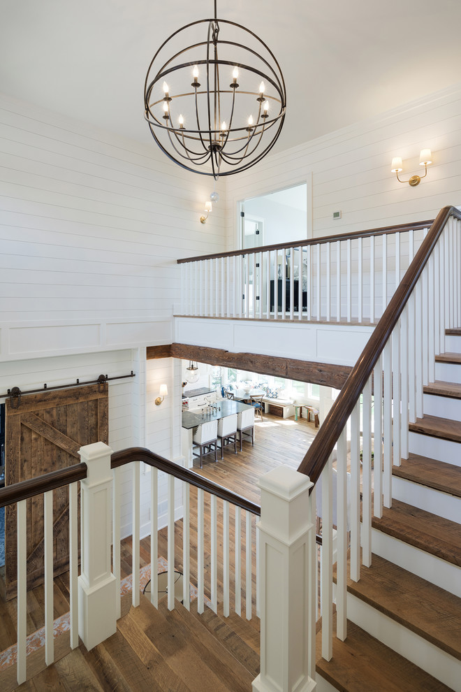 This is an example of a large beach style wood u-shaped staircase in Minneapolis with painted wood risers and wood railing.