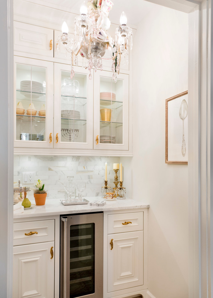 This is an example of a traditional single-wall home bar in New York with glass-front cabinets, white cabinets, white splashback and no sink.