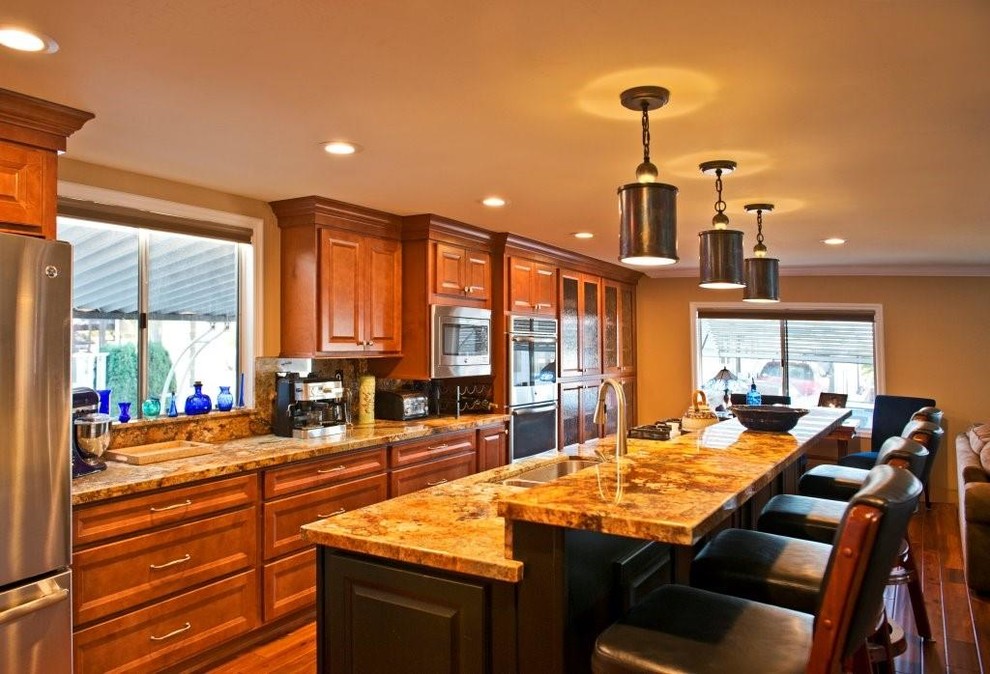 This is an example of a mid-sized transitional galley eat-in kitchen in San Diego with a double-bowl sink, raised-panel cabinets, brown cabinets, granite benchtops, multi-coloured splashback, stainless steel appliances, medium hardwood floors and with island.
