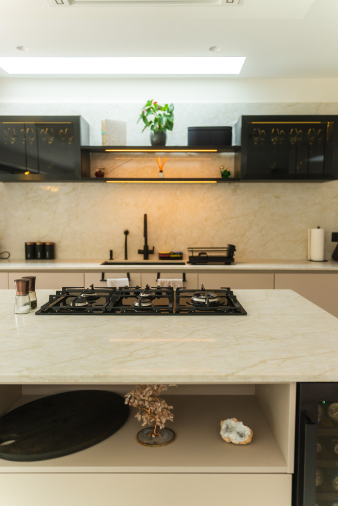 Medium sized cream and black single-wall open plan kitchen in London with beige cabinets, quartz worktops, beige splashback, engineered quartz splashback, black appliances, porcelain flooring, an island, grey floors, beige worktops and feature lighting.