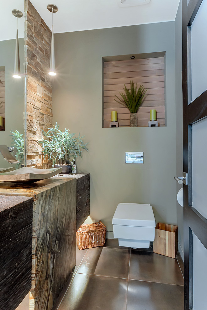 Photo of a small contemporary powder room in Minneapolis with a wall-mount toilet, stone tile, ceramic floors, a vessel sink, granite benchtops, brown floor, beige tile, green walls and flat-panel cabinets.