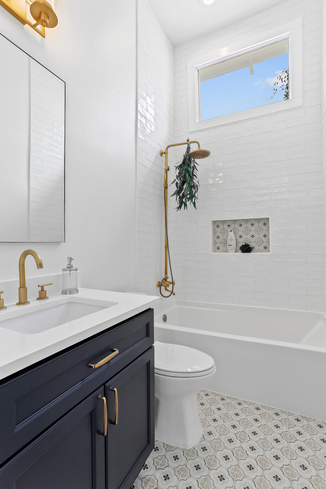 Inspiration för ett mellanstort amerikanskt vit vitt badrum för barn, med luckor med infälld panel, blå skåp, ett badkar i en alkov, en dusch/badkar-kombination, en toalettstol med separat cisternkåpa, vit kakel, keramikplattor, vita väggar, cementgolv, ett undermonterad handfat och marmorbänkskiva