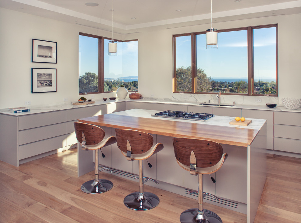 Photo of a large contemporary u-shaped open plan kitchen in Los Angeles with an undermount sink, recessed-panel cabinets, grey cabinets, marble benchtops, white splashback, stone slab splashback, stainless steel appliances, medium hardwood floors and with island.