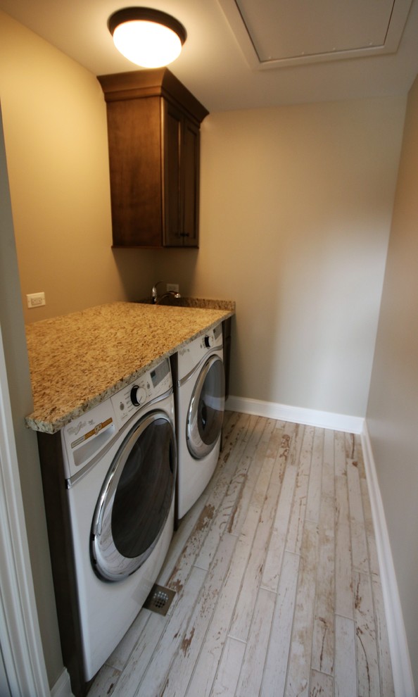 Inspiration for a small traditional single-wall dedicated laundry room in Chicago with an undermount sink, dark wood cabinets, granite benchtops, beige walls, a side-by-side washer and dryer, recessed-panel cabinets, light hardwood floors, brown floor and beige benchtop.