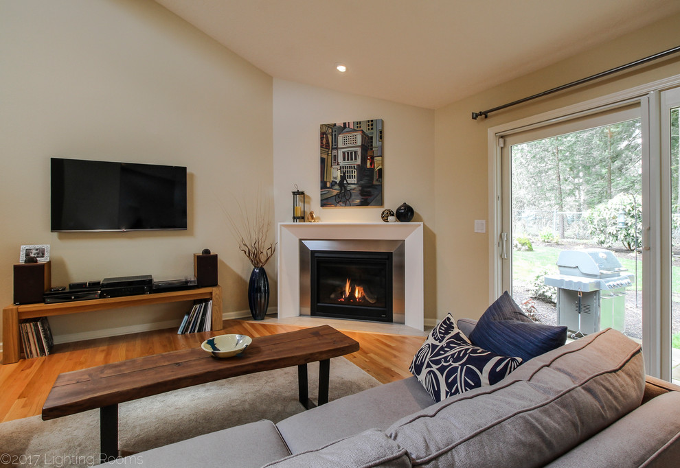 This is an example of a mid-sized contemporary formal open concept living room in Portland with beige walls, light hardwood floors, a corner fireplace, a wood fireplace surround, a wall-mounted tv and brown floor.