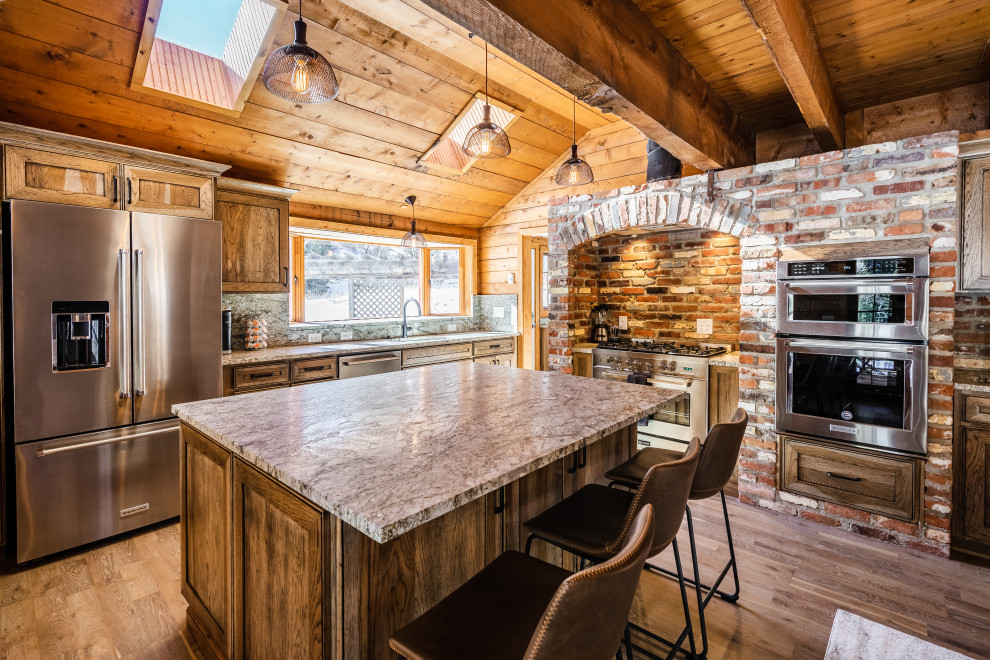 Example of a mountain style medium tone wood floor and brown floor kitchen design in Denver with an undermount sink, shaker cabinets, medium tone wood cabinets, stainless steel appliances, an island and gray countertops