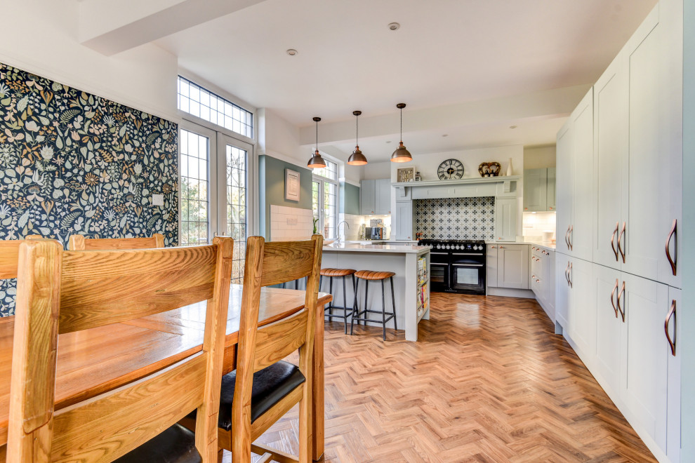 Inspiration for a large traditional grey and teal u-shaped open plan kitchen in Sussex with a belfast sink, shaker cabinets, blue cabinets, quartz worktops, white splashback, metro tiled splashback, black appliances, medium hardwood flooring, a breakfast bar, brown floors, white worktops and a chimney breast.