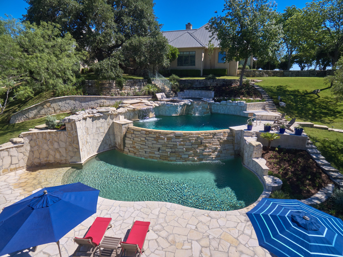 Hot tub - large tropical backyard custom-shaped and stone infinity hot tub idea in Austin