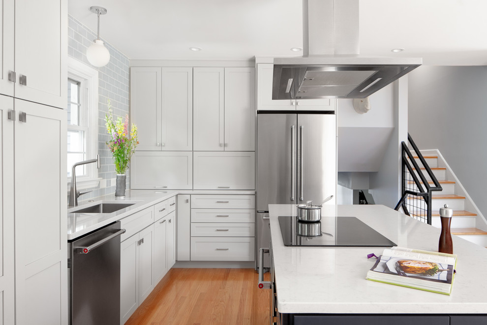 Design ideas for a small transitional l-shaped open plan kitchen in Raleigh with an undermount sink, shaker cabinets, subway tile splashback, stainless steel appliances, light hardwood floors, with island, white benchtop, grey cabinets, quartz benchtops, blue splashback and brown floor.