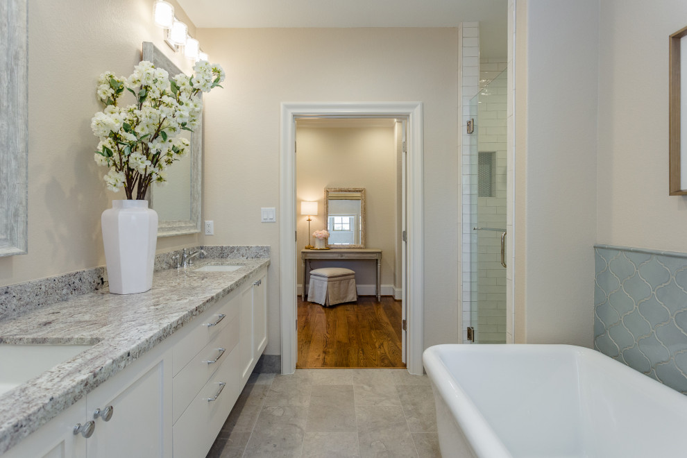 This is an example of a mid-sized arts and crafts master bathroom in Houston with shaker cabinets, white cabinets, a freestanding tub, a double shower, a two-piece toilet, beige tile, ceramic tile, beige walls, limestone floors, an undermount sink, granite benchtops, grey floor, a hinged shower door, multi-coloured benchtops, an enclosed toilet, a double vanity, a floating vanity and decorative wall panelling.