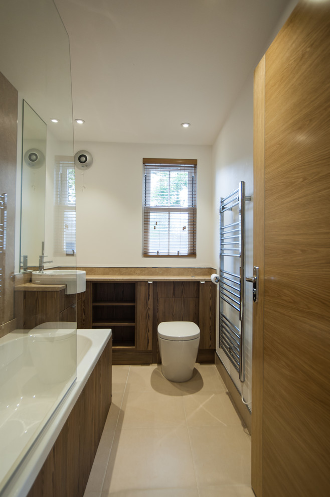 Design ideas for a small contemporary kids bathroom in Hertfordshire with flat-panel cabinets, medium wood cabinets, brown tile, wood benchtops, a drop-in tub, a corner shower, a wall-mount toilet, stone slab, white walls, ceramic floors, a drop-in sink, beige floor and a hinged shower door.