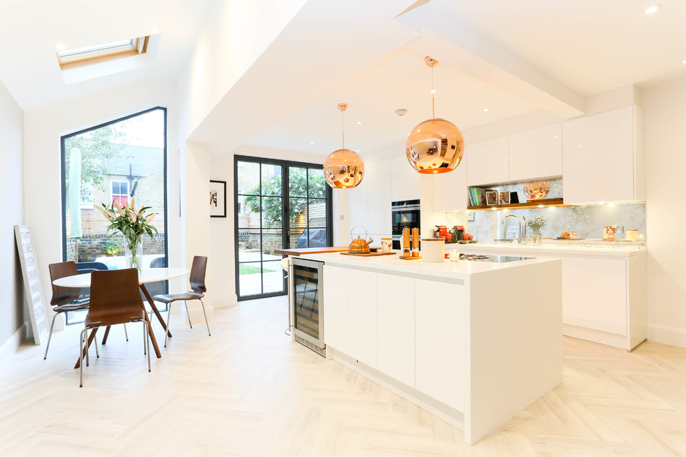 Mid-sized contemporary single-wall kitchen in London with flat-panel cabinets, white cabinets, metallic splashback, metal splashback, stainless steel appliances, with island, beige floor, white benchtop and light hardwood floors.