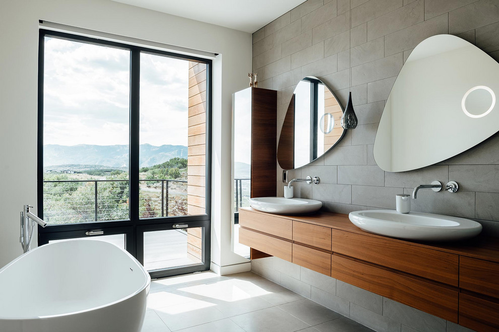 Photo of a mid-sized contemporary master bathroom in Salt Lake City with flat-panel cabinets, medium wood cabinets, a freestanding tub, gray tile, cement tile, white walls, porcelain floors, a vessel sink, wood benchtops, grey floor, brown benchtops and a double vanity.