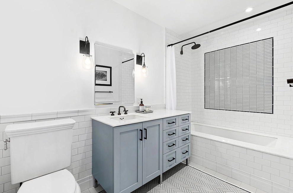 Photo of a mid-sized transitional 3/4 bathroom in Chicago with shaker cabinets, blue cabinets, an alcove tub, a shower/bathtub combo, a two-piece toilet, white tile, subway tile, white walls, porcelain floors, an undermount sink, solid surface benchtops, grey floor, a shower curtain and white benchtops.