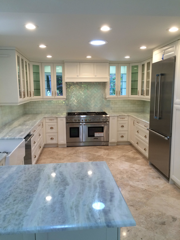Inspiration for a large transitional u-shaped open plan kitchen in Miami with a farmhouse sink, glass-front cabinets, white cabinets, quartzite benchtops, white splashback, subway tile splashback, stainless steel appliances, a peninsula and beige floor.