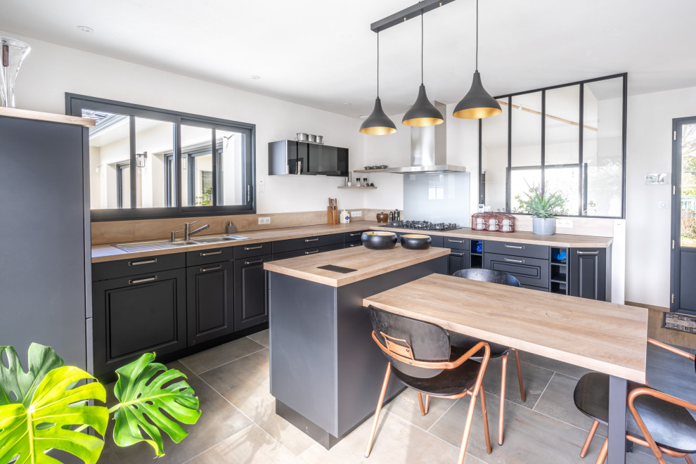 Photo of a large country u-shaped open plan kitchen in Nantes with an undermount sink, beaded inset cabinets, black cabinets, wood benchtops, beige splashback, timber splashback, panelled appliances, ceramic floors, with island, beige floor and beige benchtop.