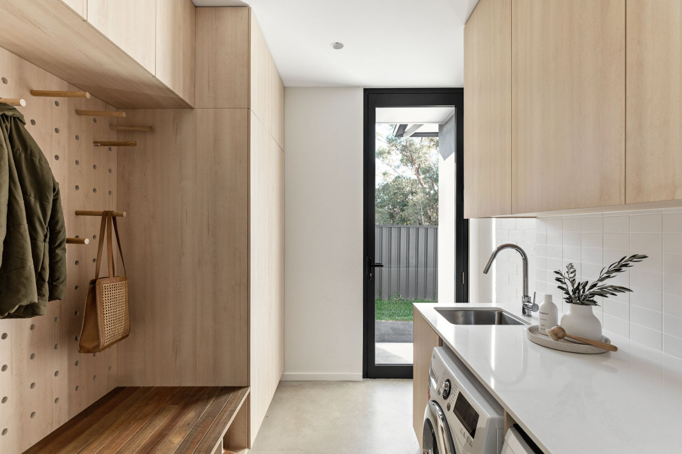 Medium sized modern galley utility room in Sydney with a submerged sink, flat-panel cabinets, light wood cabinets, engineered stone countertops, white splashback, ceramic splashback, white walls, concrete flooring, a side by side washer and dryer, grey floors and white worktops.