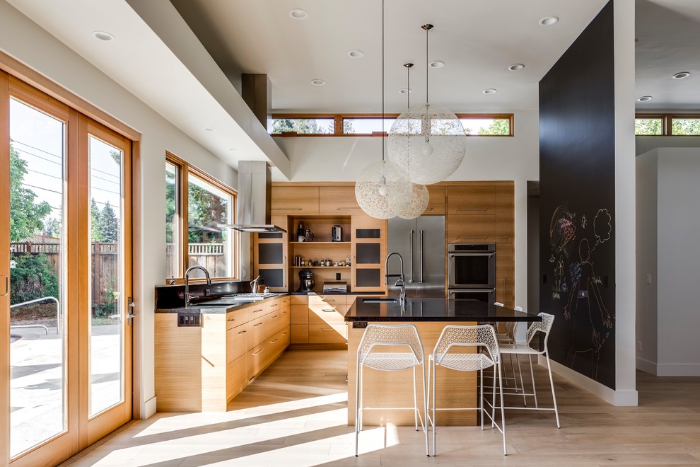 Photo of a large contemporary l-shaped eat-in kitchen in San Francisco with an undermount sink, flat-panel cabinets, medium wood cabinets, black splashback, stainless steel appliances, light hardwood floors, with island, beige floor and black benchtop.
