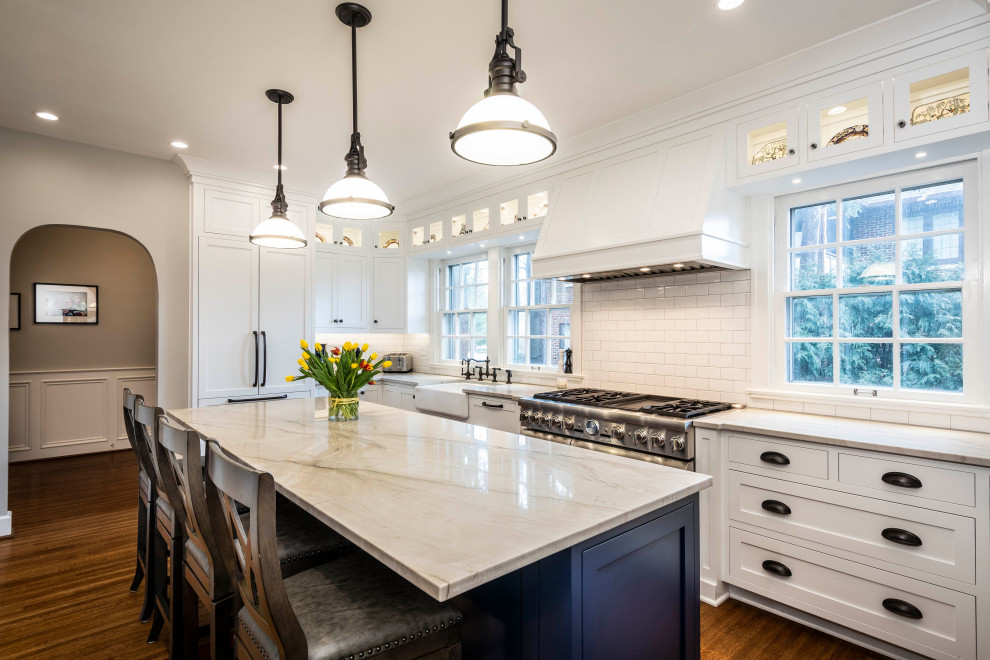 This is an example of a mid-sized transitional u-shaped kitchen in Indianapolis with a farmhouse sink, shaker cabinets, white cabinets, quartz benchtops, white splashback, panelled appliances, with island, brown floor, white benchtop, subway tile splashback and dark hardwood floors.