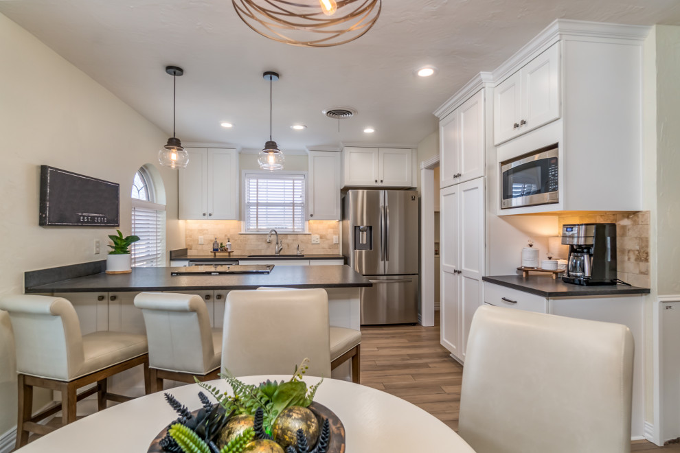 Inspiration for a transitional galley vinyl floor and beige floor eat-in kitchen remodel with a double-bowl sink, recessed-panel cabinets, white cabinets, granite countertops, beige backsplash, travertine backsplash, stainless steel appliances, a peninsula and black countertops