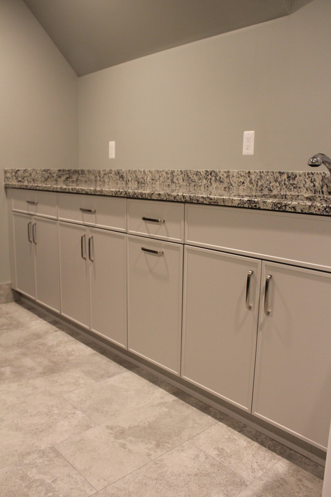 This is an example of a large modern single-wall dedicated laundry room in Detroit with shaker cabinets, grey cabinets, granite benchtops, grey benchtop, an undermount sink, grey walls, porcelain floors, a side-by-side washer and dryer and grey floor.