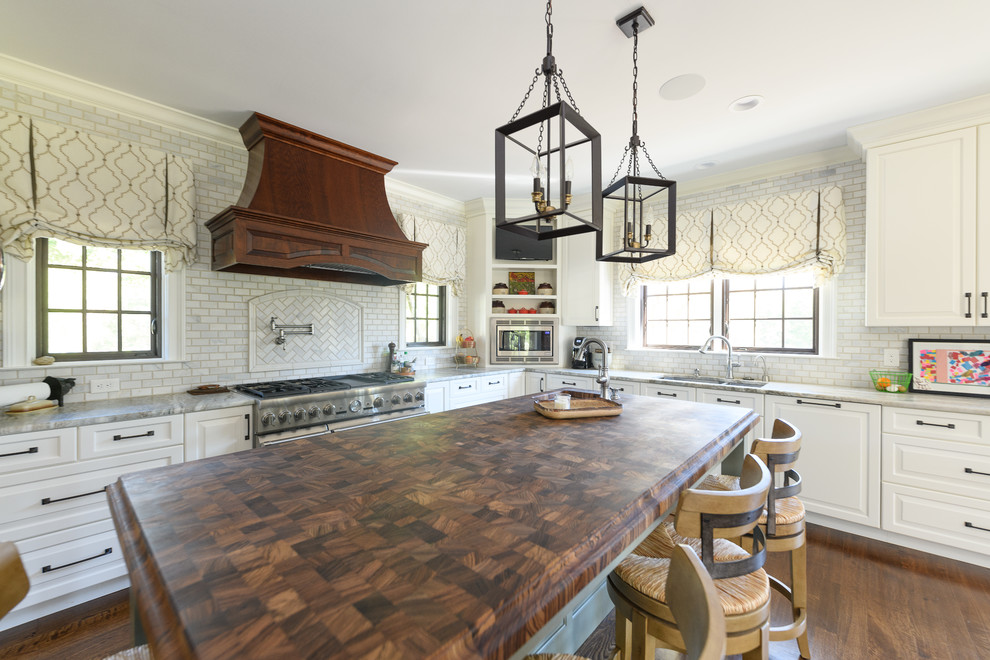 Example of a large transitional l-shaped dark wood floor and brown floor kitchen design with an undermount sink, raised-panel cabinets, white cabinets, quartzite countertops, white backsplash, marble backsplash, stainless steel appliances and an island