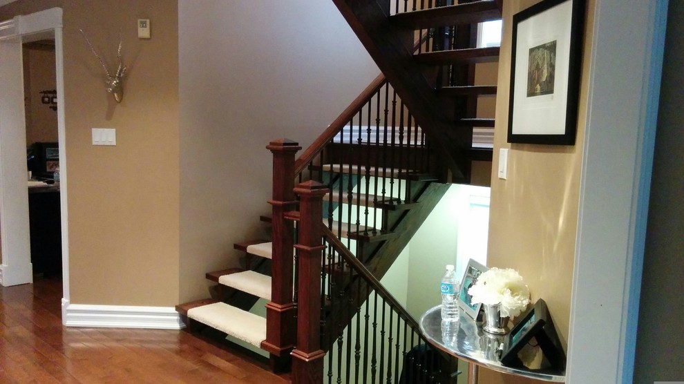 Large traditional carpeted floating staircase in Toronto with wood railing and open risers.
