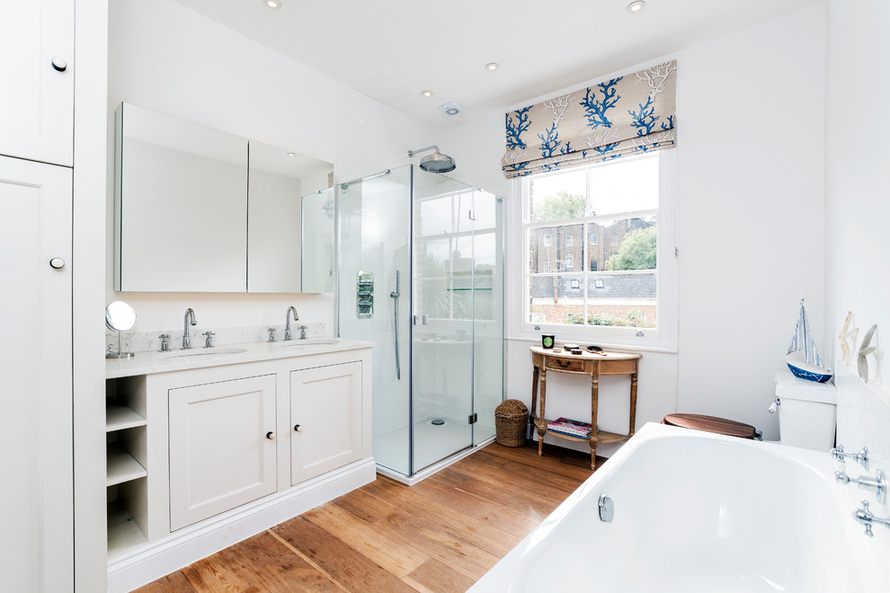 Photo of a beach style master bathroom in London with an undermount sink, shaker cabinets, beige cabinets, a corner shower, white walls and medium hardwood floors.