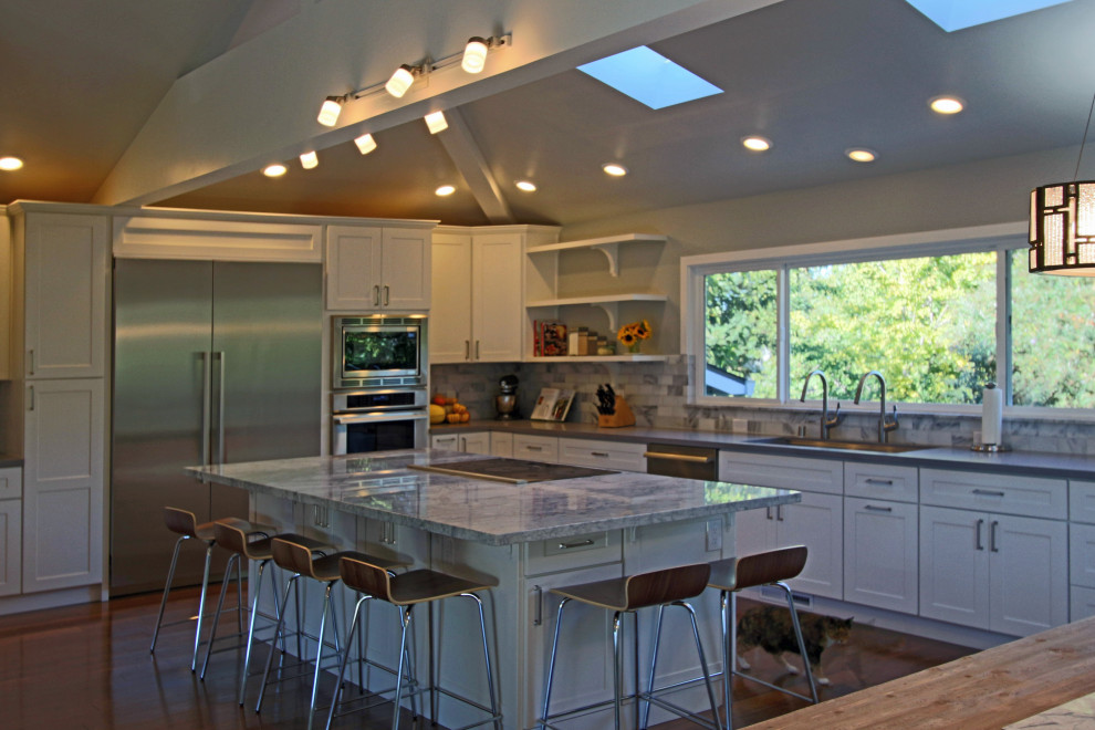 Kitchen - large u-shaped medium tone wood floor and brown floor kitchen idea with an undermount sink, shaker cabinets, white cabinets, quartzite countertops, multicolored backsplash, stone tile backsplash, stainless steel appliances, an island and multicolored countertops
