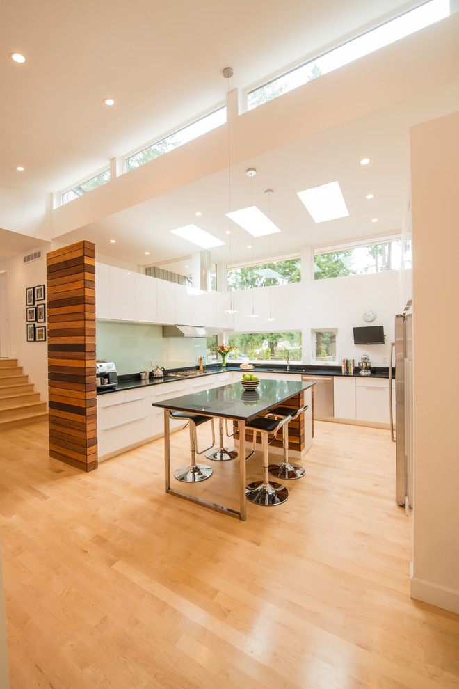 This is an example of a mid-sized contemporary l-shaped eat-in kitchen in Seattle with an undermount sink, flat-panel cabinets, yellow cabinets, granite benchtops, green splashback, glass sheet splashback, stainless steel appliances, light hardwood floors and with island.