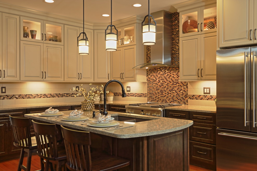 Example of a large transitional l-shaped light wood floor eat-in kitchen design with an undermount sink, raised-panel cabinets, brown cabinets, quartz countertops, beige backsplash, ceramic backsplash, stainless steel appliances and an island