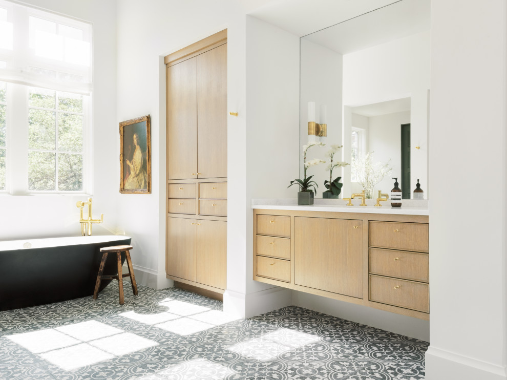 This is an example of a transitional master bathroom in Houston with light wood cabinets, a freestanding tub, white walls, multi-coloured floor and white benchtops.