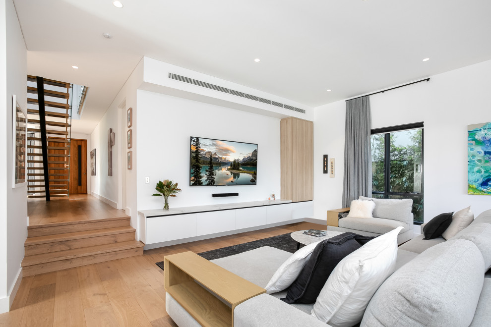 Photo of a mid-sized contemporary open concept family room in Sydney with white walls, medium hardwood floors and a wall-mounted tv.