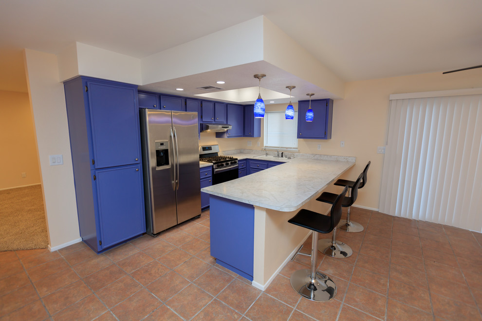 Mid-sized transitional u-shaped open plan kitchen in Los Angeles with an undermount sink, recessed-panel cabinets, blue cabinets, marble benchtops, stainless steel appliances, ceramic floors, a peninsula and brown floor.