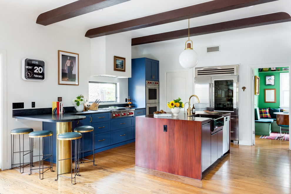 Photo of a contemporary l-shaped kitchen in Other with a farmhouse sink, shaker cabinets, soapstone benchtops, black splashback, stone slab splashback, stainless steel appliances, medium hardwood floors, with island, blue cabinets and brown floor.