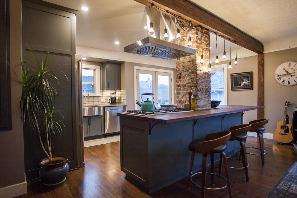 Open concept kitchen - small transitional l-shaped dark wood floor and brown floor open concept kitchen idea in Seattle with a farmhouse sink, shaker cabinets, gray cabinets, stainless steel appliances, an island, beige countertops, granite countertops, white backsplash and porcelain backsplash