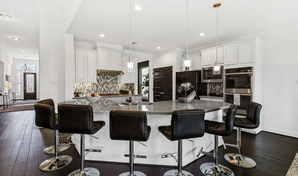 Design ideas for a mid-sized transitional l-shaped open plan kitchen in Houston with an undermount sink, shaker cabinets, white cabinets, quartzite benchtops, grey splashback, mosaic tile splashback, black appliances, light hardwood floors, with island, brown floor, grey benchtop and coffered.