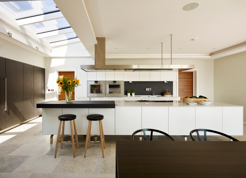 This is an example of a large contemporary galley eat-in kitchen in Devon with flat-panel cabinets, white cabinets, black splashback, stainless steel appliances, with island and quartzite benchtops.