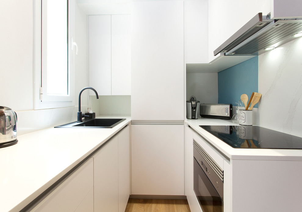 Design ideas for a small contemporary u-shaped open plan kitchen in Barcelona with flat-panel cabinets, white cabinets, white benchtop, quartz benchtops, white splashback, marble splashback, panelled appliances, medium hardwood floors, no island, brown floor and a drop-in sink.