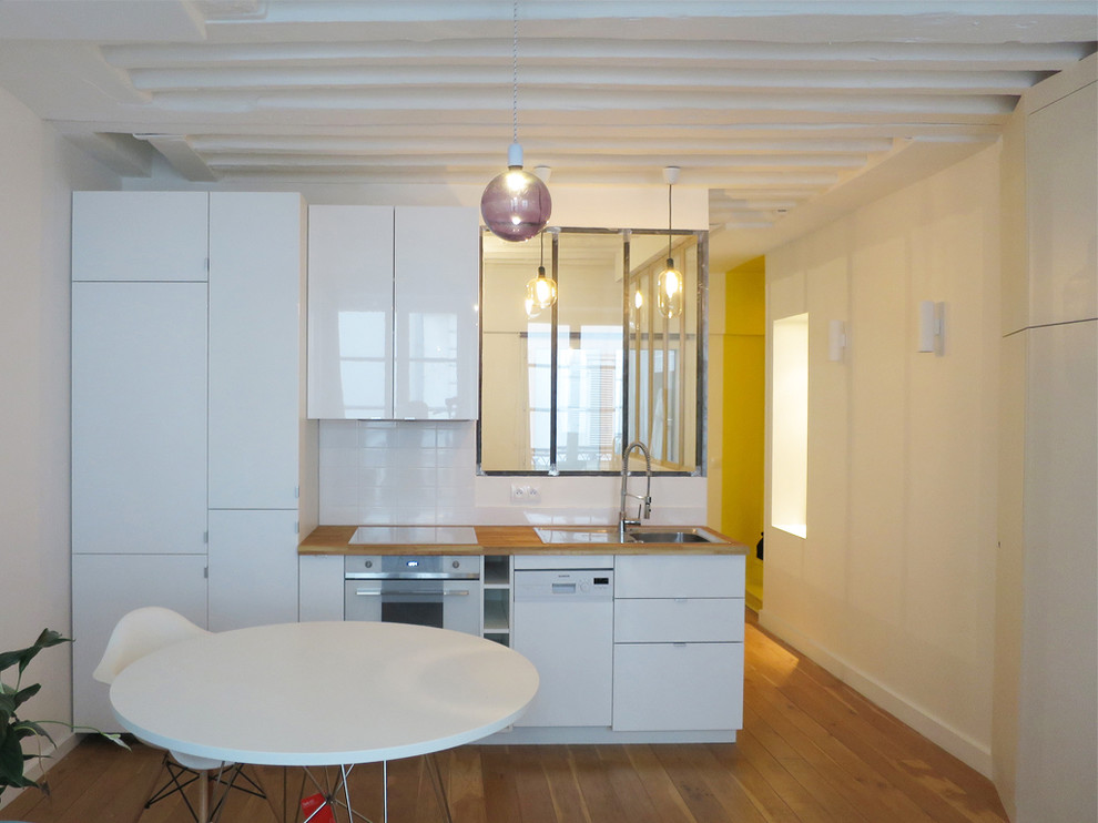 Small contemporary single-wall open plan kitchen in Paris with a single-bowl sink, beaded inset cabinets, white cabinets, wood benchtops, white splashback, porcelain splashback, white appliances, no island and medium hardwood floors.