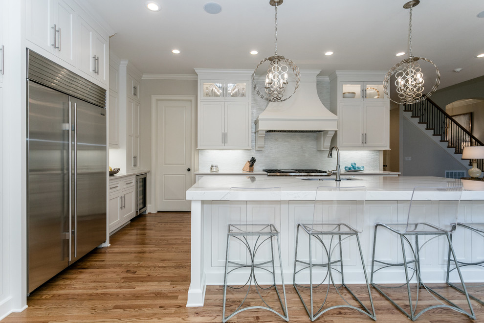 Eat-in kitchen - transitional l-shaped medium tone wood floor and brown floor eat-in kitchen idea with a double-bowl sink, white cabinets, quartz countertops, stainless steel appliances, an island, white countertops, recessed-panel cabinets and gray backsplash